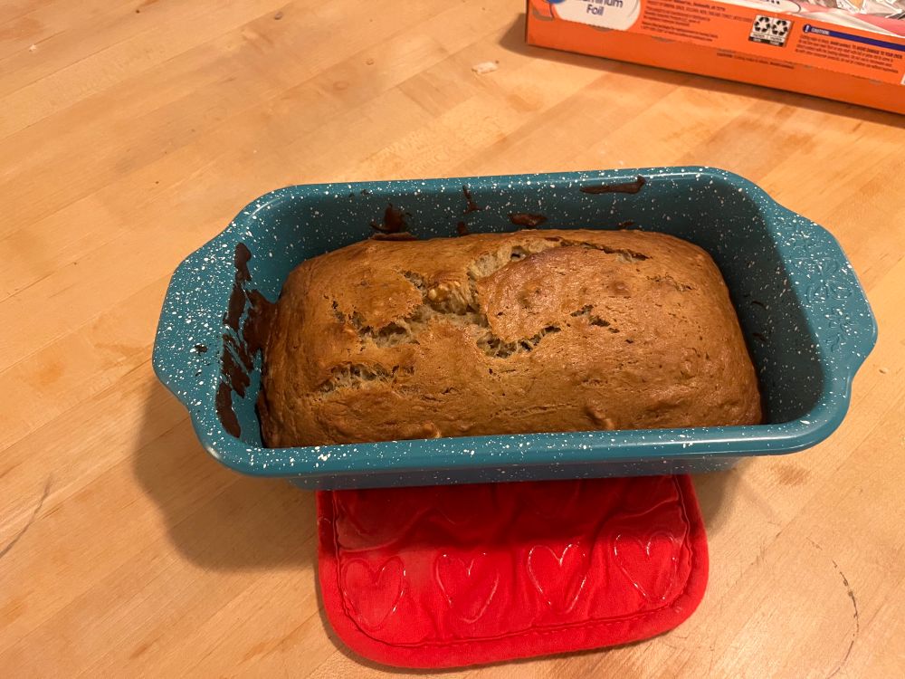 a blue bread tin on a table with cooked banana bread in the tin
