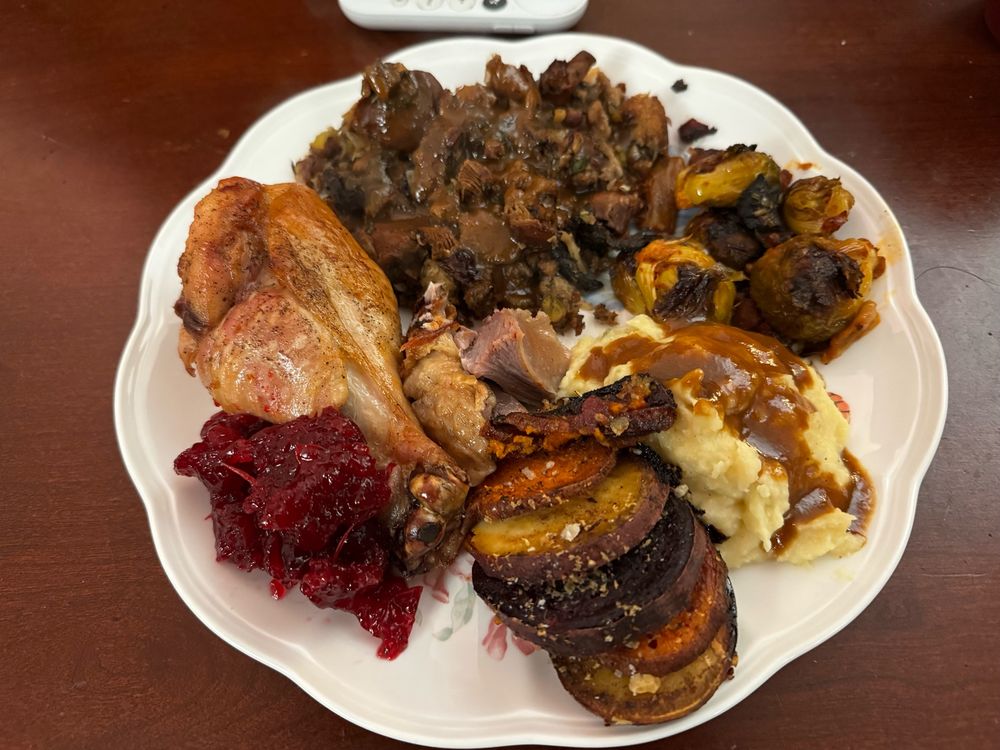 A plate of thanksgiving dinner; turkey, stuffing and gravy, homemade cranberry sauce, sliced candied sweet potatoes, with creamy mashed potato and kimchi brussel sprouts