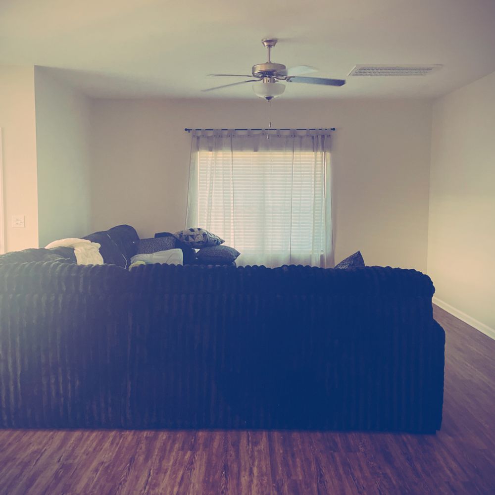 Picture of a black fuzzy couch with gray linen curtains in cream colored living room with a barnwood floor. 