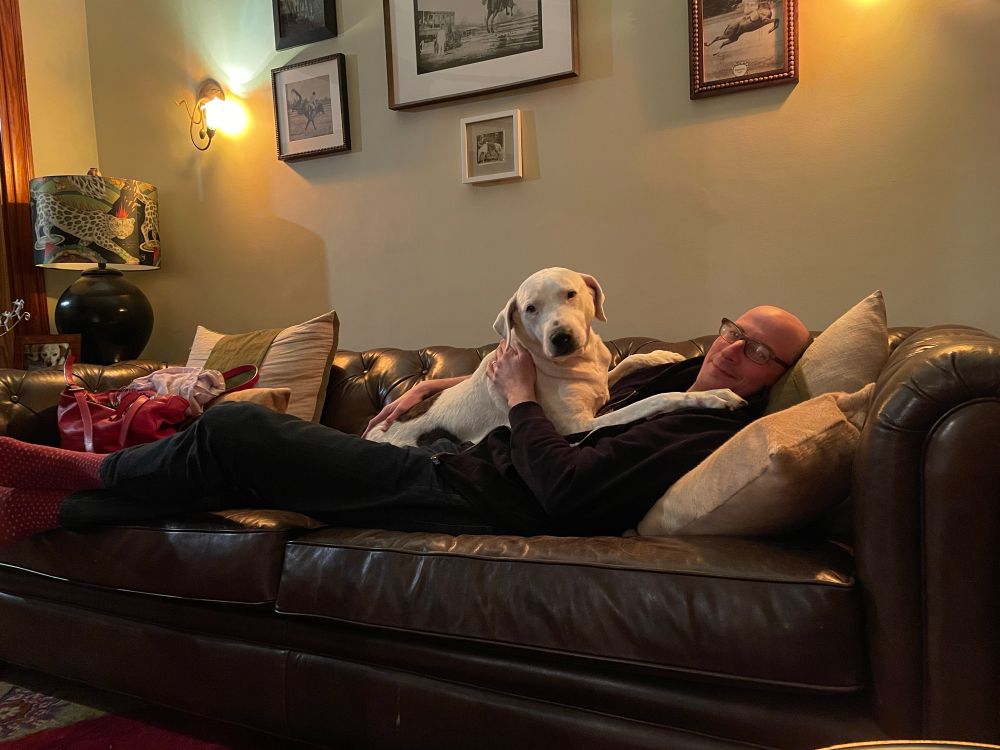 Me lying on a big leather couch at an Airbnb with Charlie splayed out on top of me looking like Krypto
