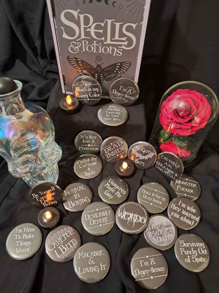 A bunch of gothic and occult themed pins featuring different sayings laid out with some spooky decorations.