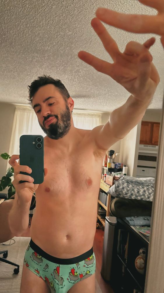a bearded man in patterned briefs takes a mirror selfie