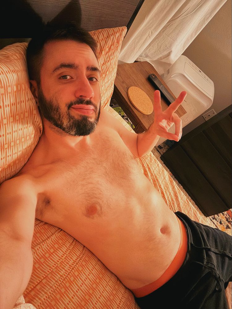 shirtless selfie in bed of a bearded man
