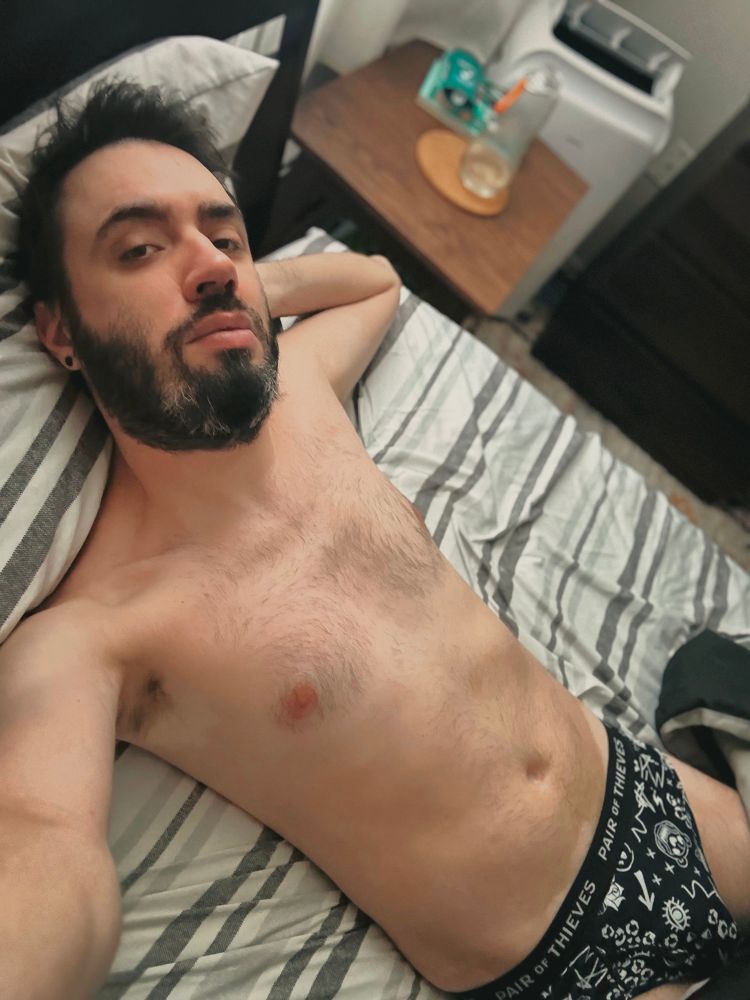 bed selfie. i’m shirtless in patterned black briefs, one hand behind my head