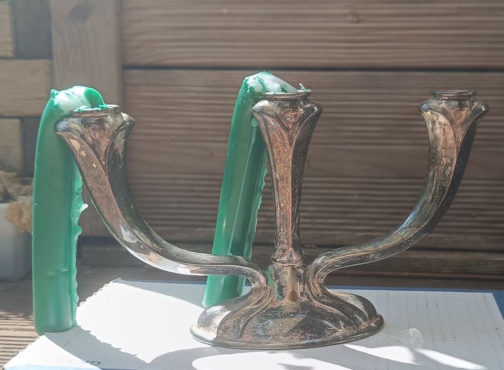 Alter silberner Dreier-Kerzenleuchter mit zwei grünen Kerzen, die zur Seite davongeschmolzen sind 