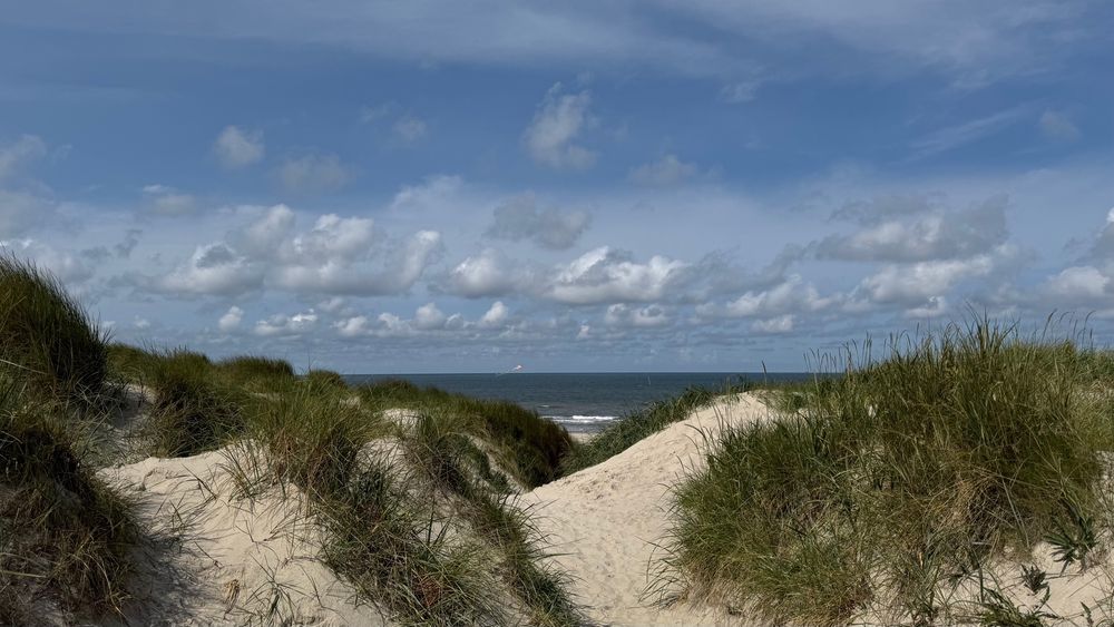 Dünen mit Block zum Meer und schönen Wollen am blauen Himmel.