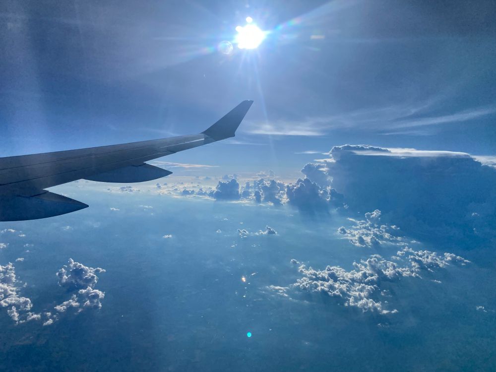 Photo of clouds and sunshine over an airplane wing, in flight