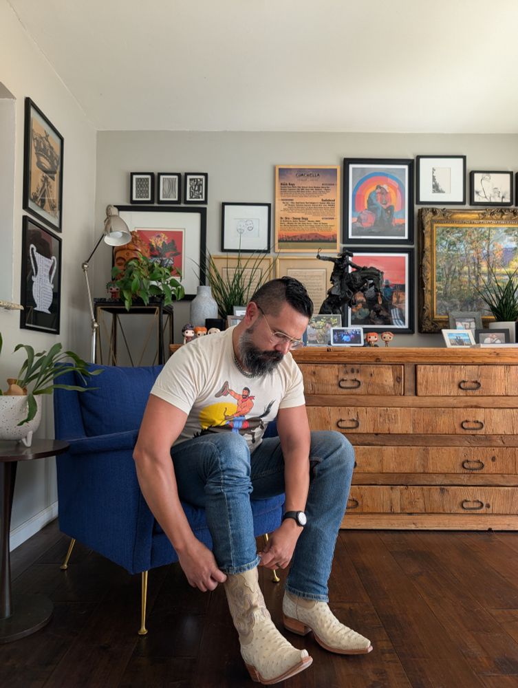 Jorge sitting in a blue chair pulling down his jeans over a pair of white ostrich cowboy boots