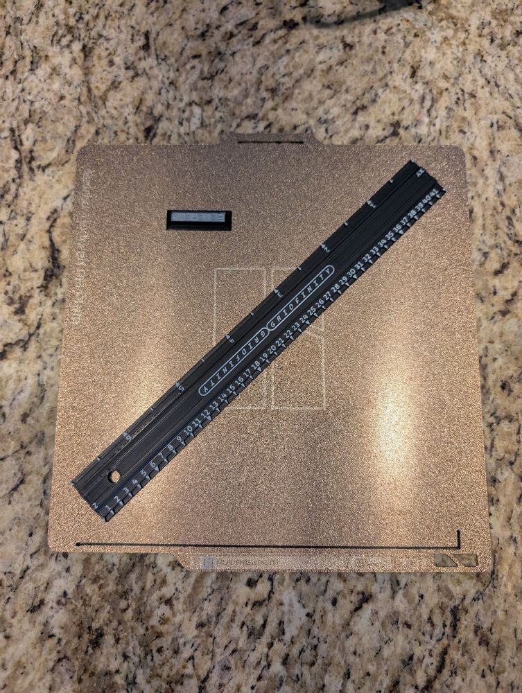 A Bambu Labs print plate on a kitchen counter with a black ruler with white lettering.