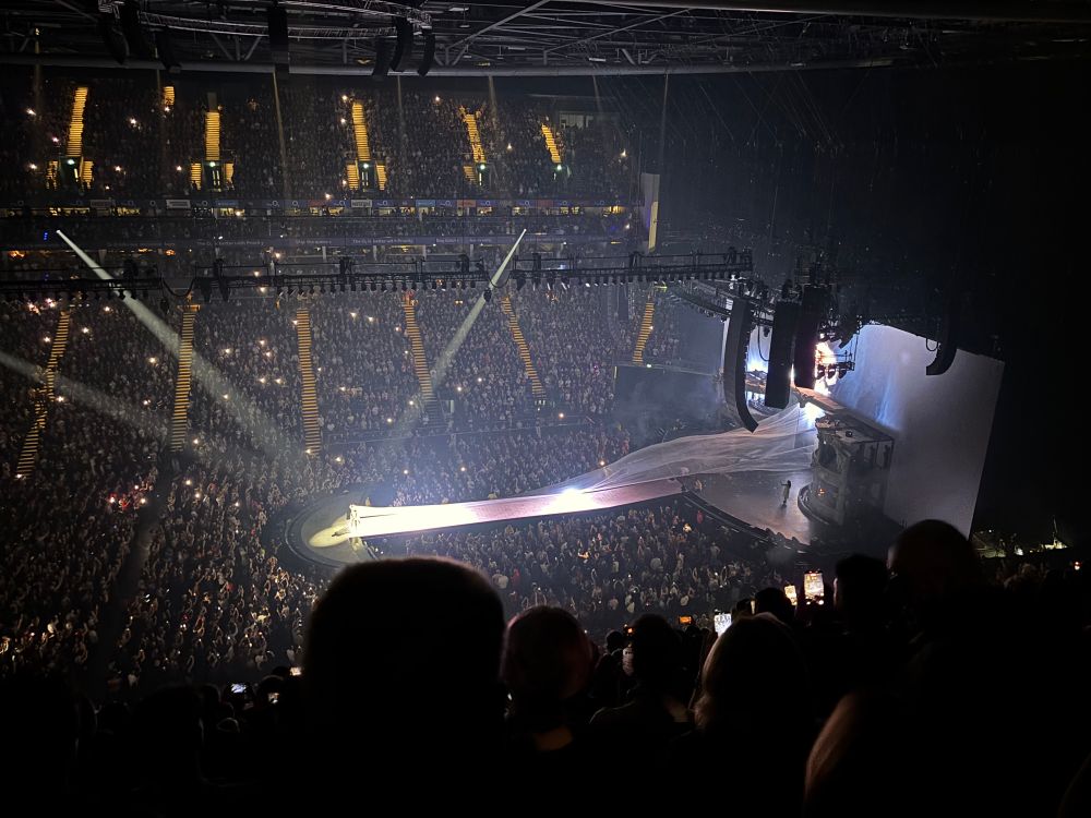 Photo of the Lady Gaga concert at the o2 Arena taken from the right. Image shows Gaga at the end of a runway dressed in white, with a white train flowing the extent of the runway.