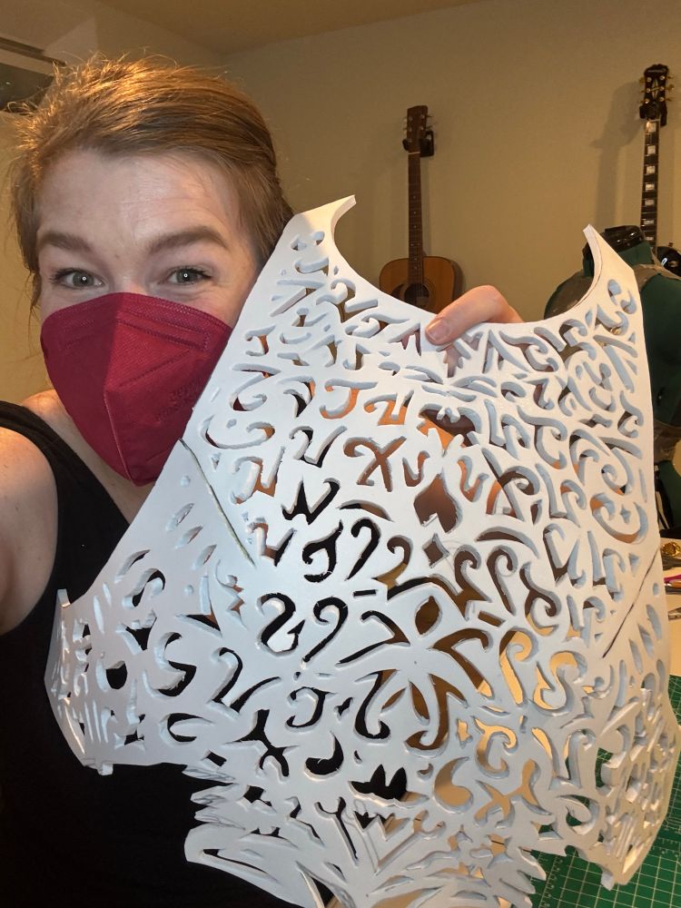 Me wearing a red mask and ponytail holding up an unpainted EVA foam breastplate armor with designs, many of which old tongue or Wheel of Time inspired, carved into the foam.