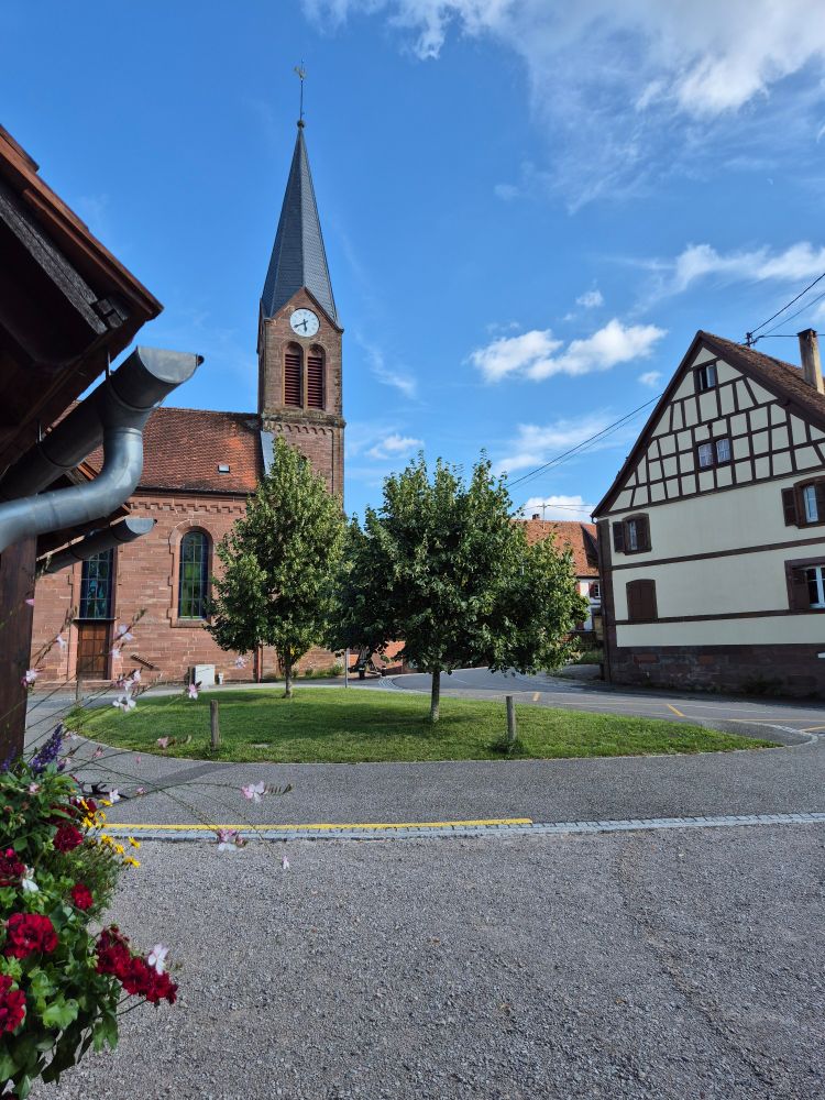 Kirche, davor ein kleiner Platz, rechts ein Fachwerkhaus 