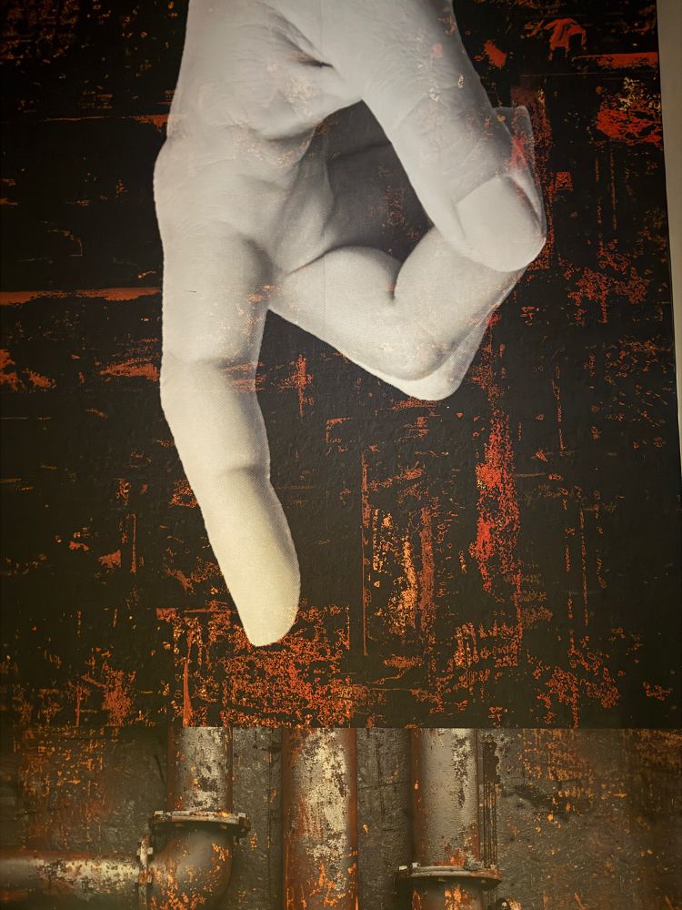 huge wall art piece of a large centered white-colored hand pointing downard and industrial black and red and rust colored background.