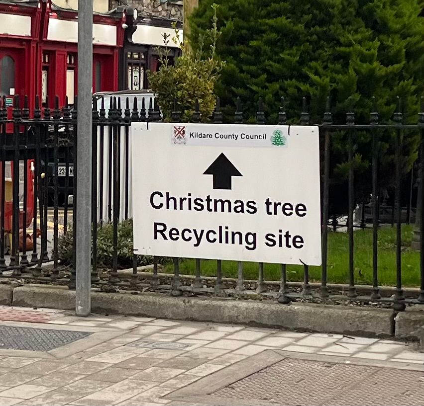 Printed sign tied to metal fence, reading “Christmas tree recycling site”