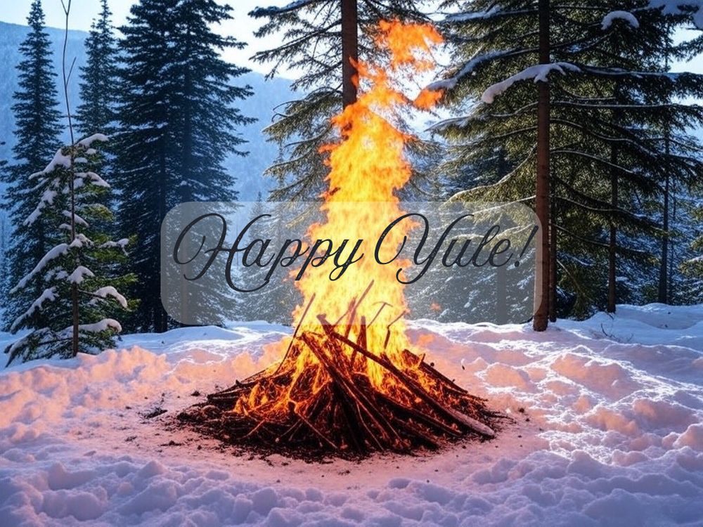 An AI-generated large bonfire blazes in a snowy winter forest setting, with tall snow-covered evergreen trees in the background. The flames rise dramatically against the blue-tinted winter landscape. The text "Happy Yule" is overlaid in an elegant script font across the center of the image. The snow around the bonfire reflects the warm orange glow of the flames, creating a striking contrast between the cold winter scene and the warmth of the fire.