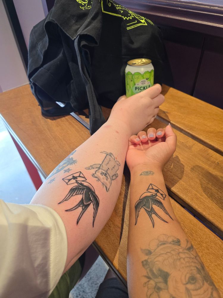 two arms with flipped versions of the same bird tattoo holding a love note. 