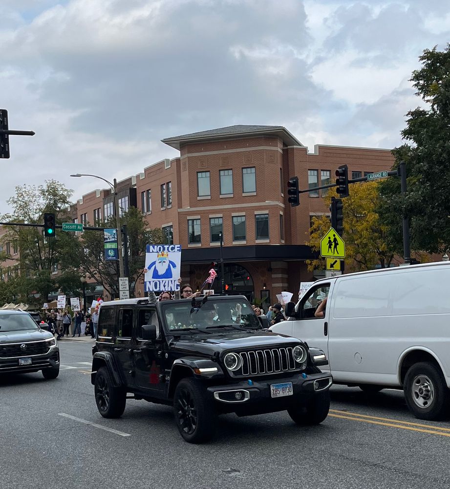 A passenger in a Jeep is holding a sign through the sun roof. The sign says: No Ice No King. Another passenger is waving 2 American flags.