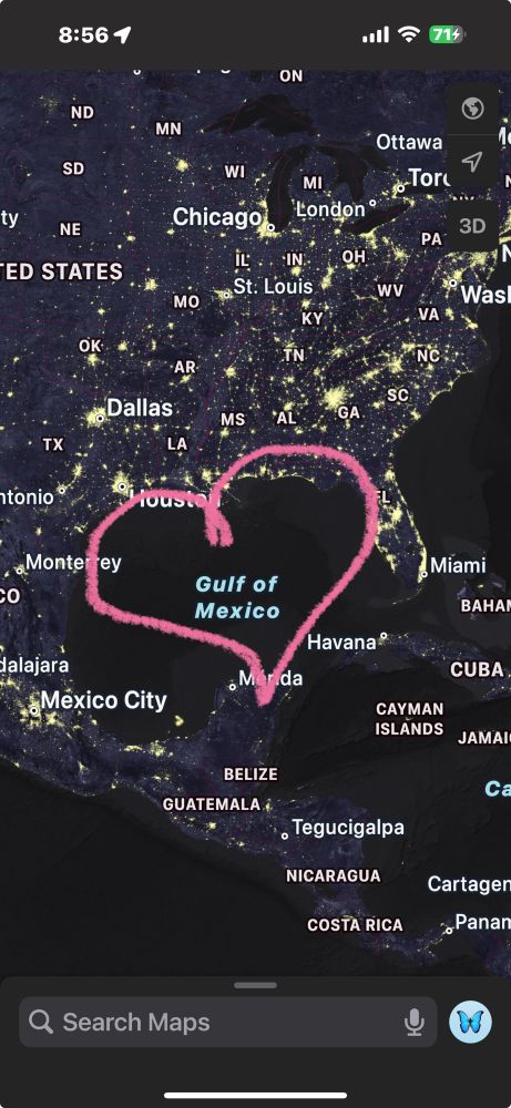 The image is a screenshot of a nighttime satellite view from a maps application, displaying the Gulf of Mexico and surrounding regions, including the southern United States, Mexico, and parts of Central America. Major cities such as Chicago, Dallas, Houston, and Mexico City are visible, illuminated by their night lights. Over the Gulf of Mexico, a pink hand-drawn heart encircles the body of water. The interface elements of the map app are visible, including a search bar at the bottom and navigation buttons on the right side. The device's status bar at the top shows the time as 8:56, along with Wi-Fi and battery indicators.