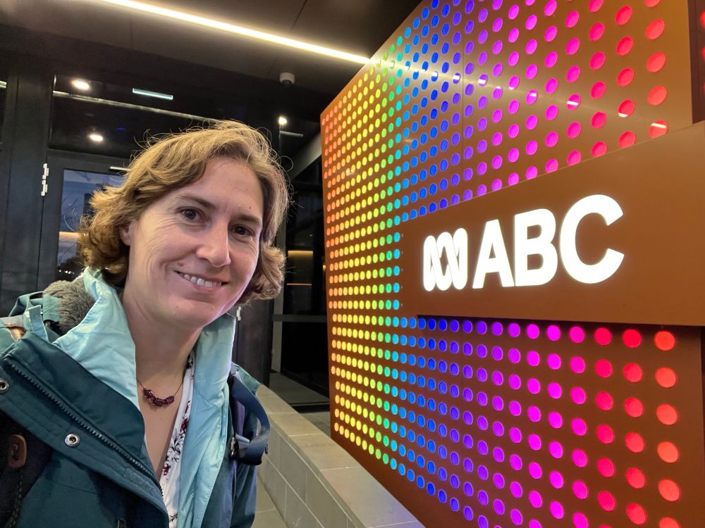 Me in a big coat smiling next to a bright multicolored wall with little lights and the ABC logo