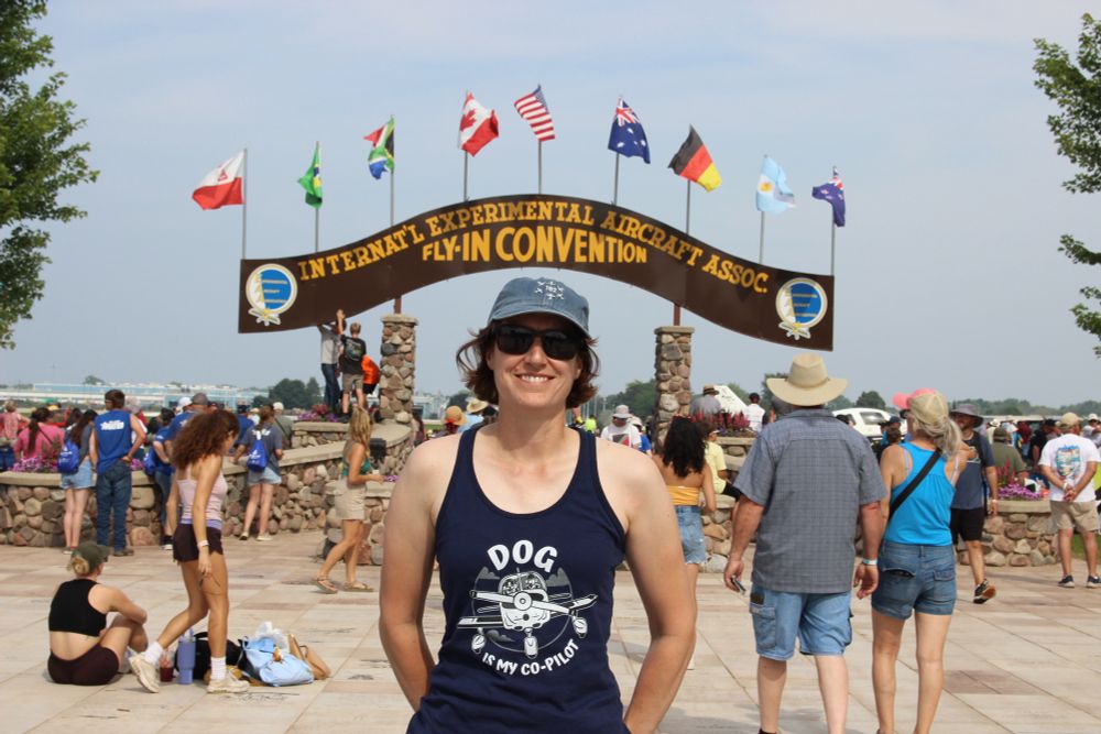 Me standing in front of the big show arch at Oshkosh AirVenture wearing a tank top that says “Dog is my co-pilot”. The image on the shirt is a cartoon of a low-wing airplane in which there is a human in the left (pilot) seat and a happy goofy dog in the right (copilot) seat