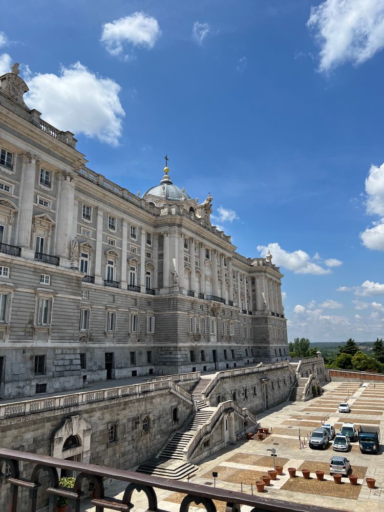 An elegant palace with some cars parked in front of it, with blue sky behind 