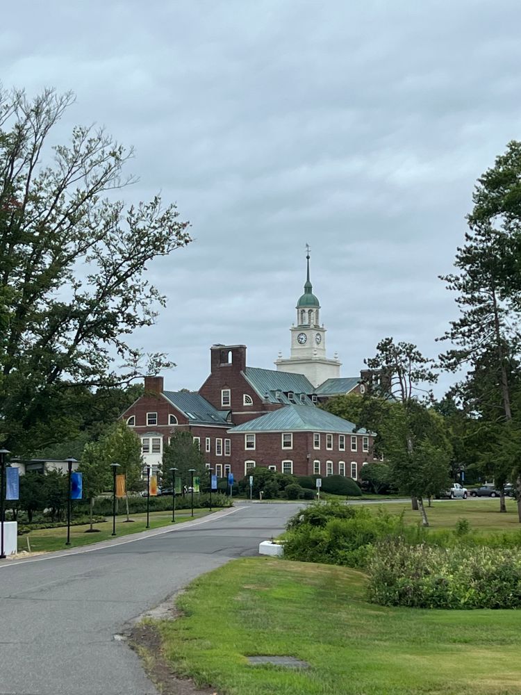 The main buildings of the Institute at the end of a driveway. There are several stately red brick buildings and a white tower in the middle, with trees all around 