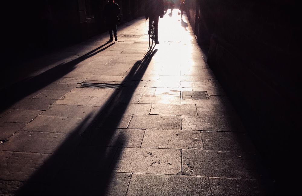 Backlit walkway with long shadows of pedestrians and a cyclist.