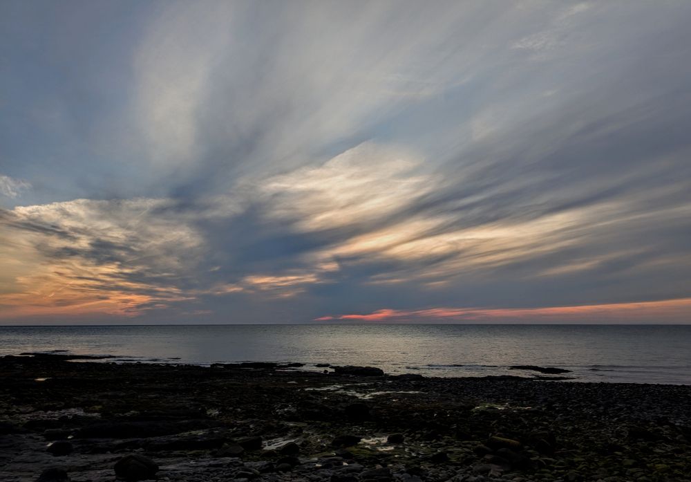 A dramatic sunset over the ocean with a rocky coastline in the foreground