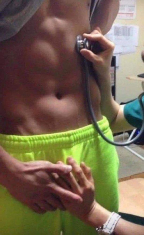 imagem de um homem com a camisa erguida enquanto alguém coloca um estetoscópio na barriga de tanquinho dele enquanto segura com a mão bem cheia no pau do indivíduo. ele está com a mão por cima da mão de quem, aparentemente, o examina. a foto não mostra o rosto de nenhum dos dois.