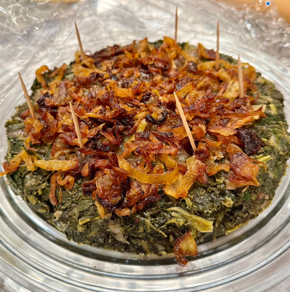 hindbeh-- a layer of spinach cooked with caramelized onions, dressed with lemon and olive oil, topped with fried/caramelized onions (photographed on a glass dish). this one is nearly finished, will be wrapped and gets another full layer of fried onions over the entire top before serving with pita.