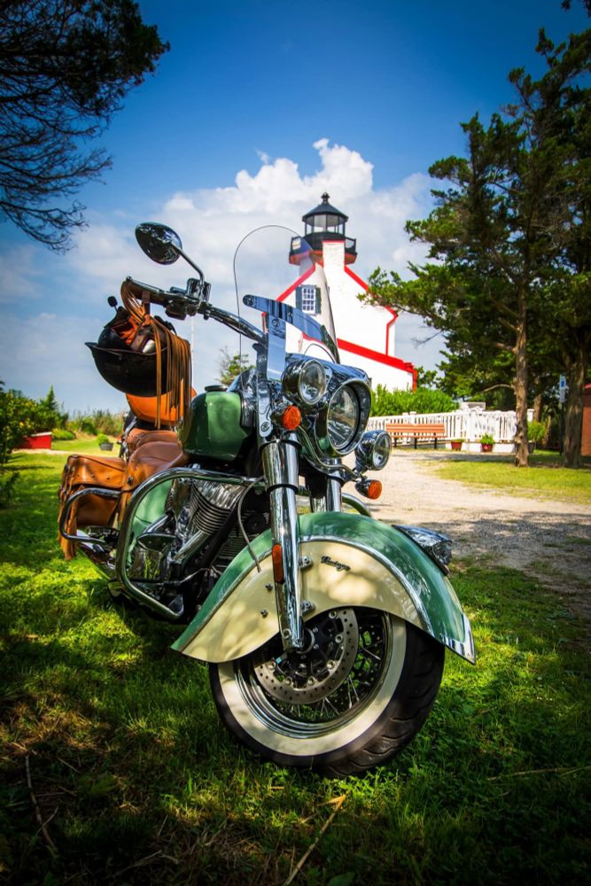 Motorcycle parked in front of a lighthouse. 