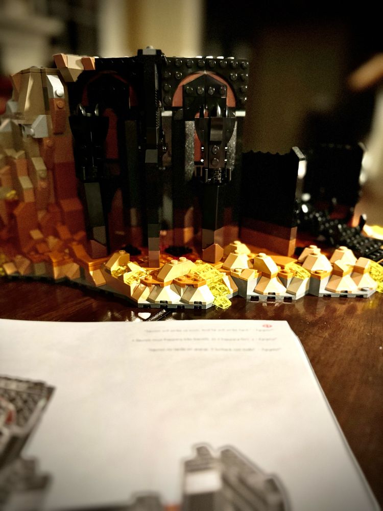 An instruction manual in front of a partial build of Barad-dûr legos. 