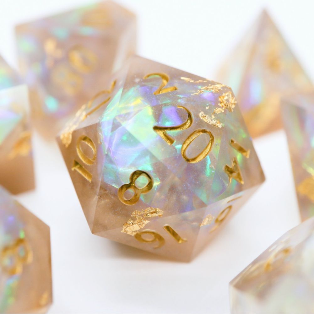 Another closeup of the D20. The dice are all cream colored with foil within that reflects hues of green and purple. The numbers on the dice are white and there are gold flakes in the dice.