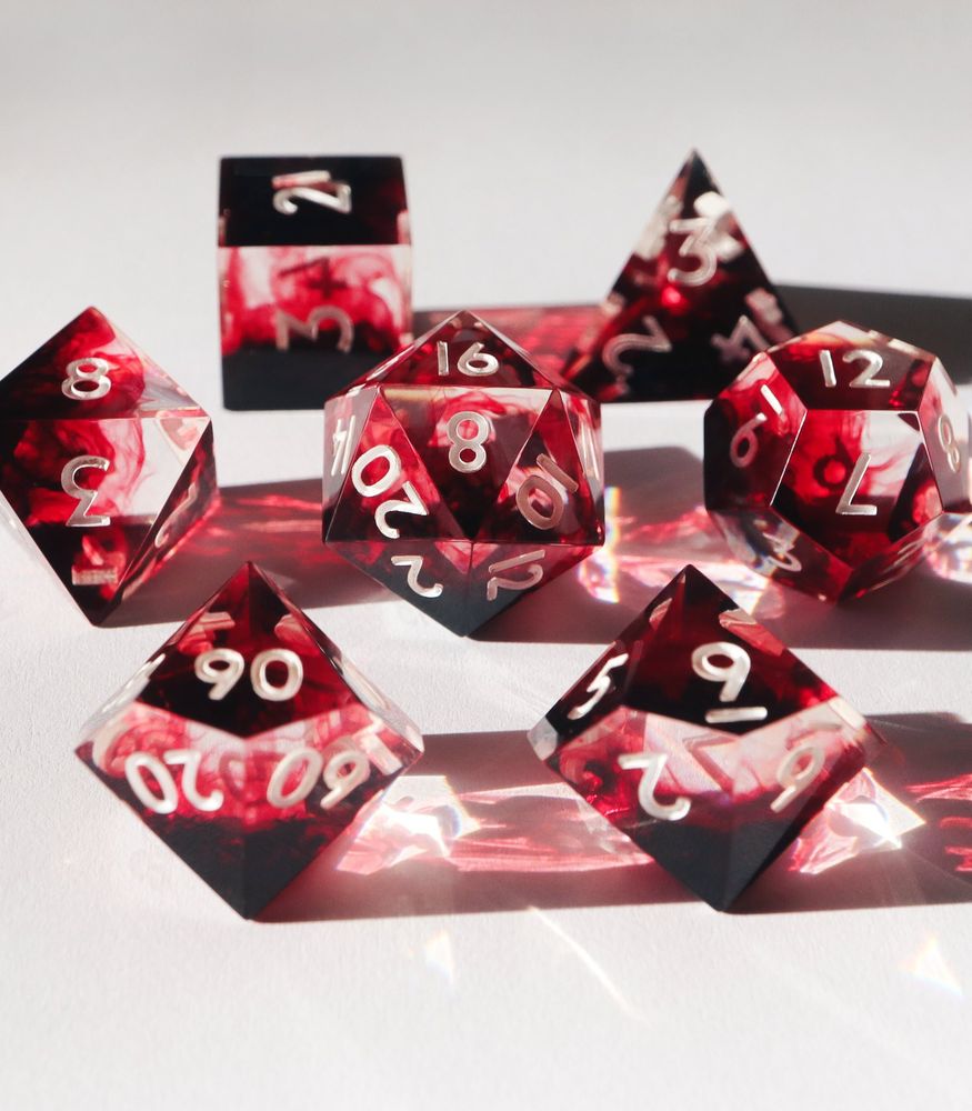 Full set of Persephone's Fury on a white background with the D20 in the middle. All the dice are clear resin with red pools from one side and gives a smokey blood-in-water look as it swirls through the clear portions. The numbers on the dice are white.