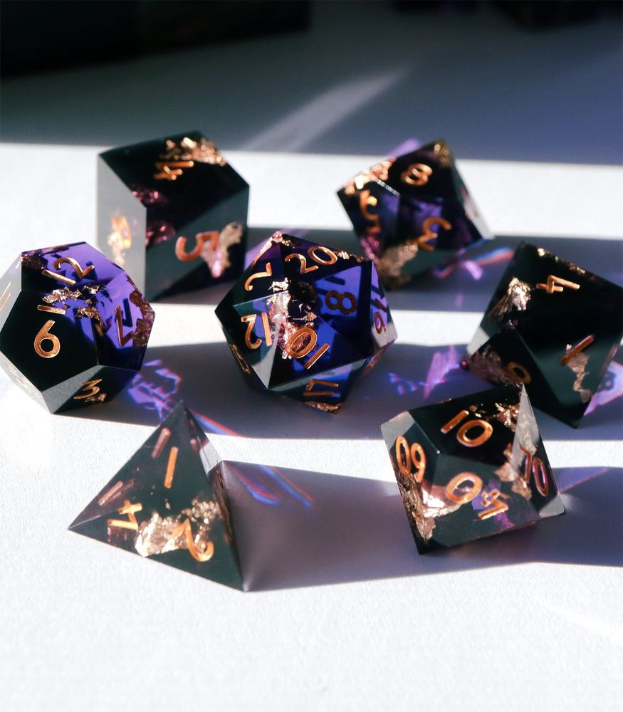 Full set of Heretic's Glory 7 piece gaming dice set on a white background. All the dice are a dark black resin with a slight purple ombre and golf leaf throughout. The numbers on the dice are gold.