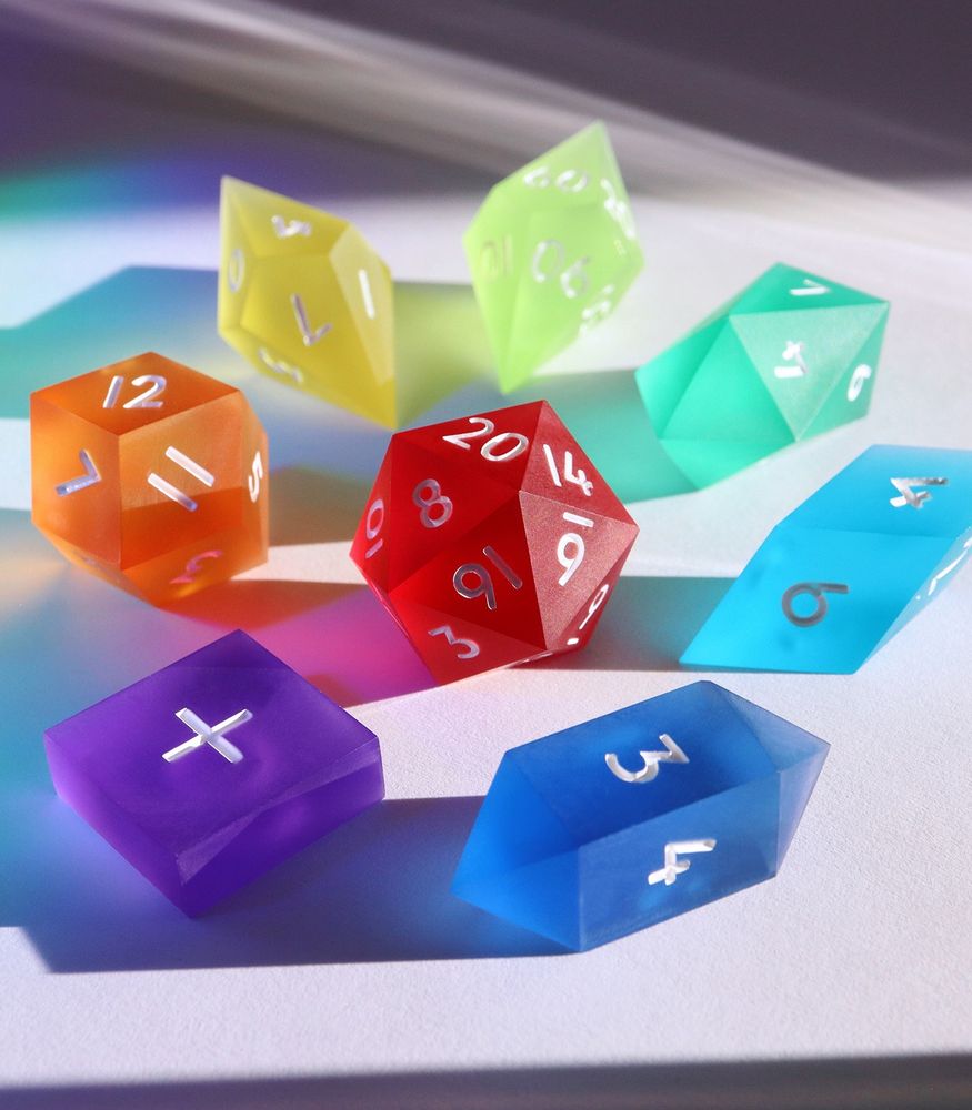 Full set of Prismatic Sea Glass arranged in a circle with the D20 in the center. The dice are frosted matte crystal shapes each in a different color of the rainbow. There are 8 total.