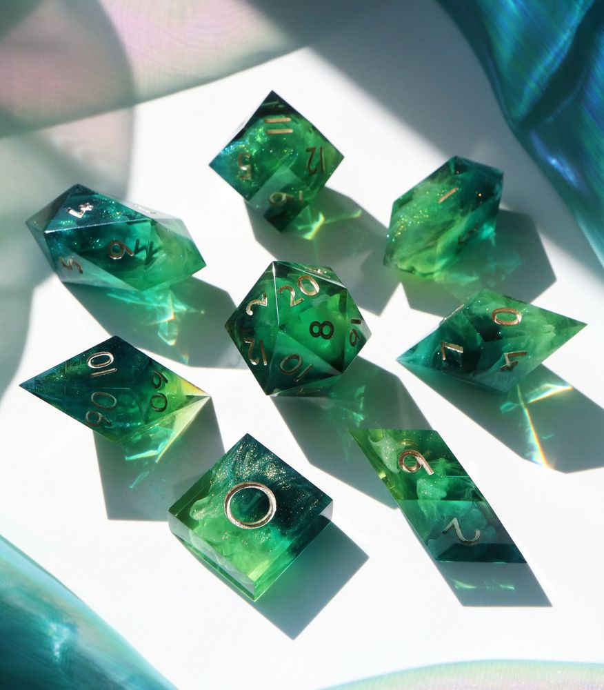 Full set of Critical Role's Residuum Dice Set arranged in a circle with the D20 in the center. The dice are a mix of light and dark green resin that swirls together with sparkle inclusions, made to resemble crystals of refined residuum. The numbers on the dice are gold.