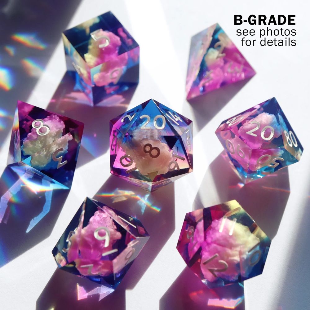 Full set of Air Ashari set arranged in a circle with the D20 in the center. All the dice are a mixed gradient of pink, yellow, and blue resin with a floating cloud inclusion. The text reads “B-Grade see photos for details”