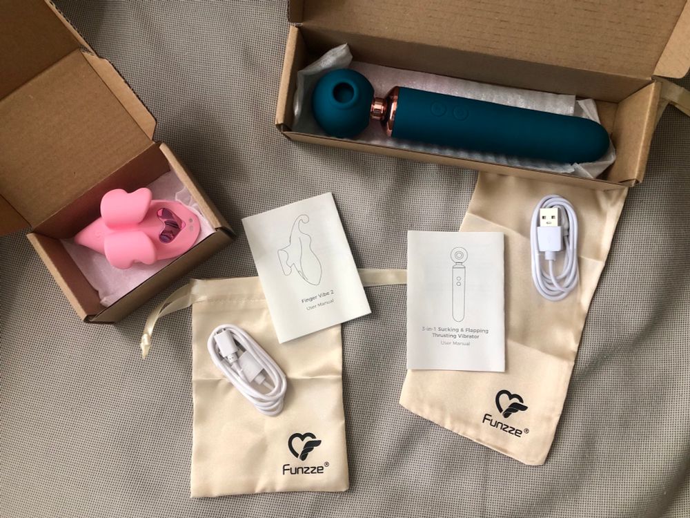 The photos is looking down on a great fabric background, with two open boxes containing adult toys. One is the finger vibe 2 - it has the shape of a butterfly and is a vibrant pink colour. The second provide is the 3 in 1 Sucking & Flapping Thrusting Vibrator - which is an ocean blue colour, long and slender, with a “ball” at the end, with a “sucker” indented into the ball. The photos also shows two note cards with the names of the products, two gold bags (to store the toys) with the Funzze logo, and a white charger for each. 
