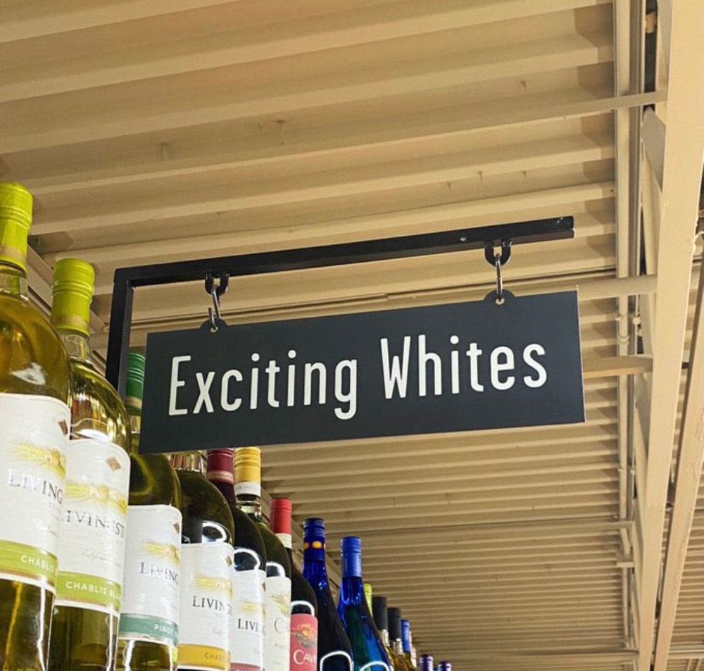 A sign above a grocery shelf filled with white wine bottles reads: exciting whites 