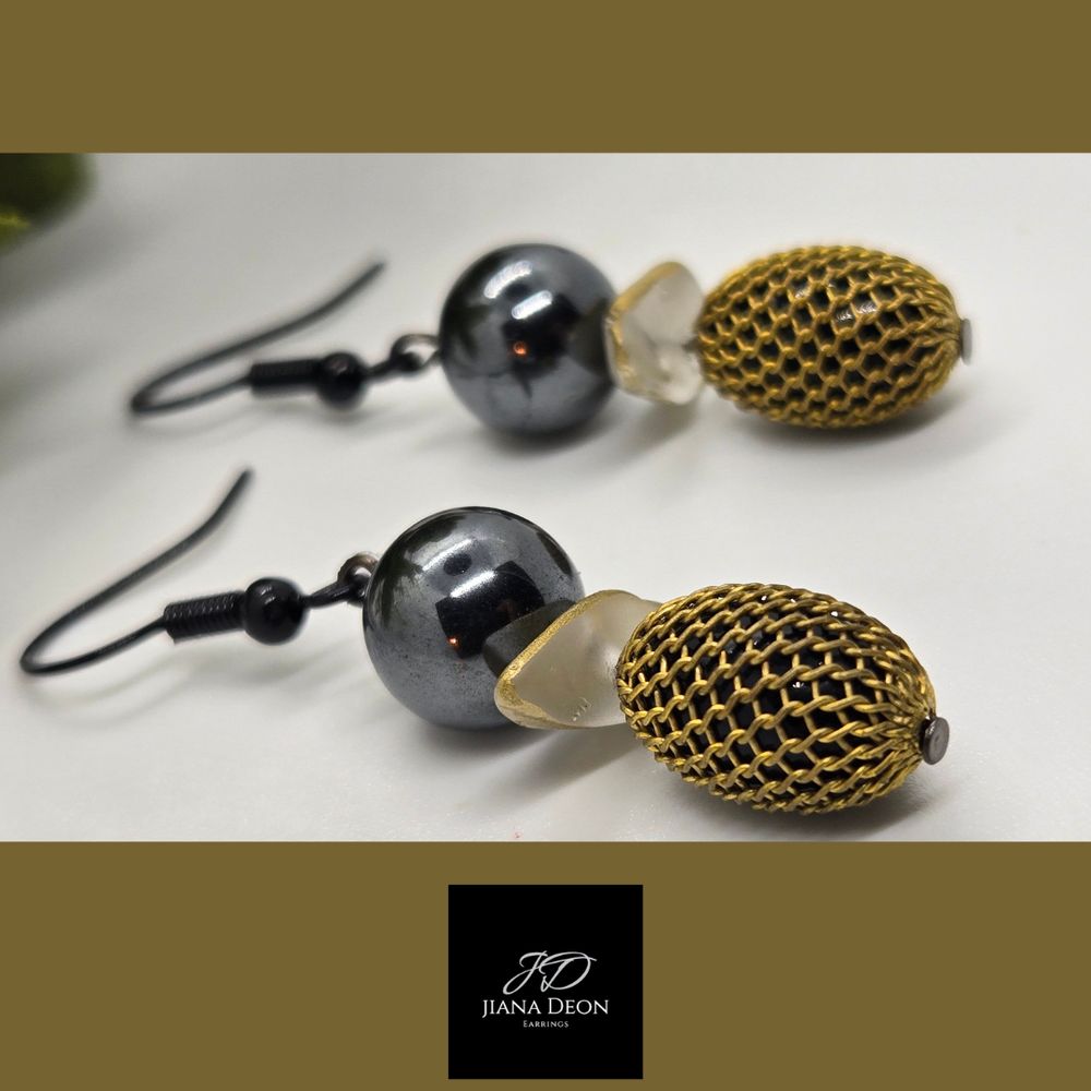 These earrings feature a unique and eclectic design with a vintage flair. These earrings are mixed materials and textures, creating a visually interesting look. A large, round black bead is at the top, followed by a delicate painted white shell. The bottom section features a gold-tone mesh link, adding a touch of texture and dimension.