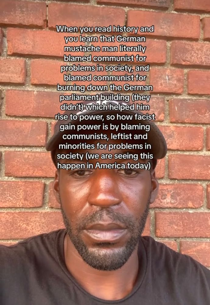 A screenshot of a TikTok of a Black man with text that reads "when you read history you learn that German mustache man literally blamed communist for problems in society, and blame communist for burning down the German parliament building (they didn't) which helped him rise to power, so how fascist gain power is by blaming communists, leftist and minorities for problems in society (we are seeing this happen in American today)"