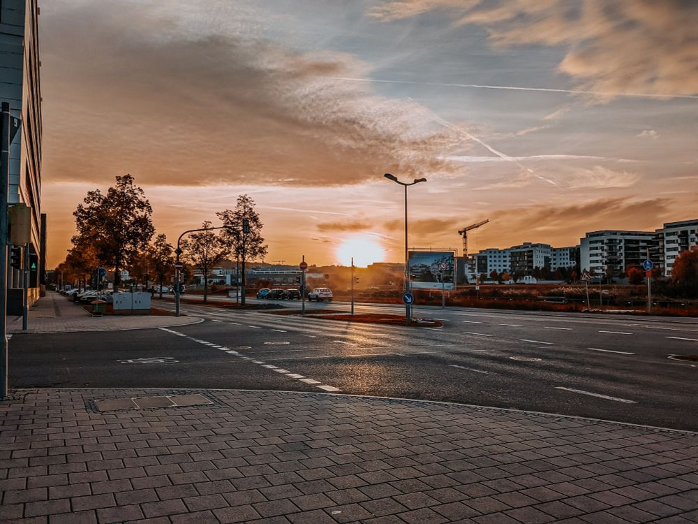 Sonnenaufgang über ein paar Häusern. Die sterile Atmosphäre der Häuser kontrastiert mit der warmen Sonne und die harten Kanten der Gebäude mit der weichen Struktur der Wolken am Himmel