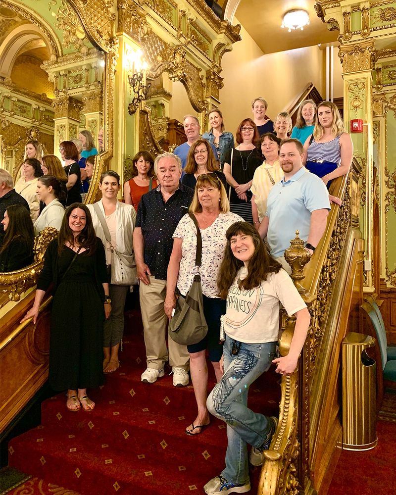 Group of people standing on the Colonial Grand Staircase, inside the ornate and luxurious interior of a theater.