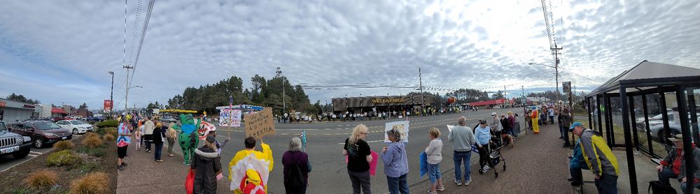 A panoramic photo of the No Kings protest in Lincoln City Oregon on Oct 18, 2025. The image shows hundreds of people lining both sides of the highway through town holding protest signs opposing Donald Trump's unconstitutional abuses of his authority.
