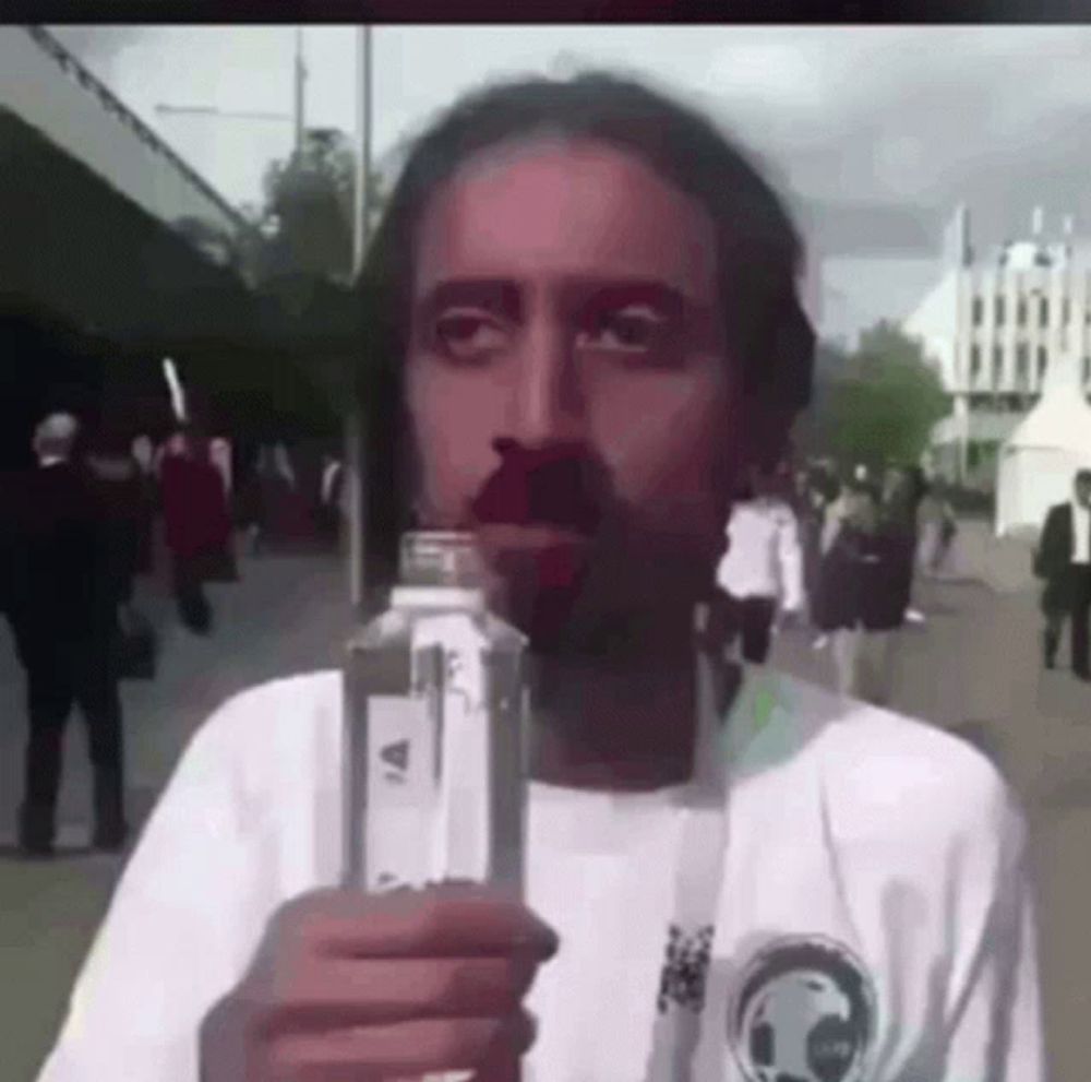 a man with a beard is holding a bottle of water in front of his face .