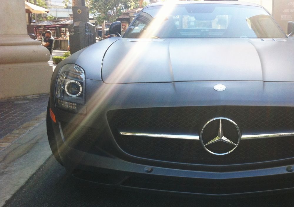 Photo of a matt black Mercedes AMG GT Coupe. Taken from the front of the car, the shot is offset to one side and interrupted by a shaft of light coming diagonally across the picture.