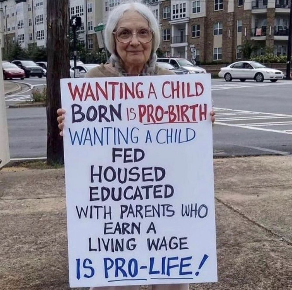 An older woman with white hair holding a protest sign that says:

Wanting a child born is pro-birth. Wanting a child fed, housed, educated, with parents who earn a living wage is pro-life.