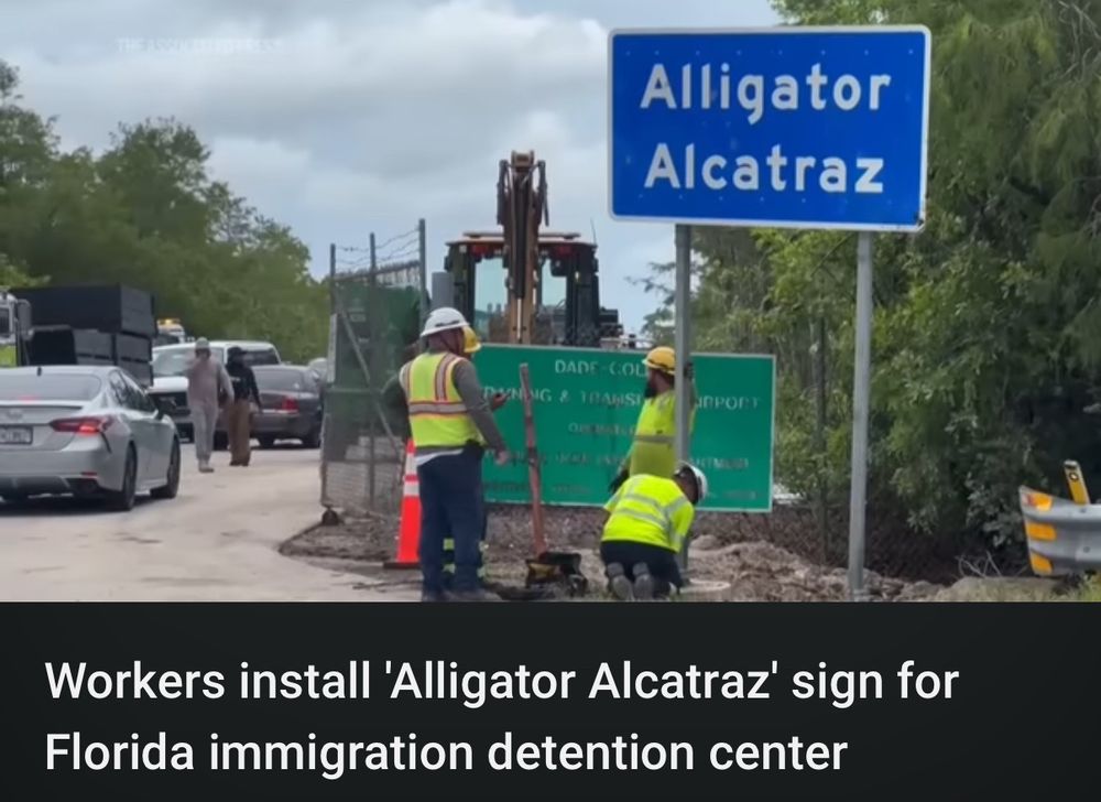 Screenshot from YouTube of a video titled “Workers install 'Alligator Alcatraz' sign for Florida immigration detention center.” 

The frame of the video is the Alligator Alcatraz sign with workers next to it. 