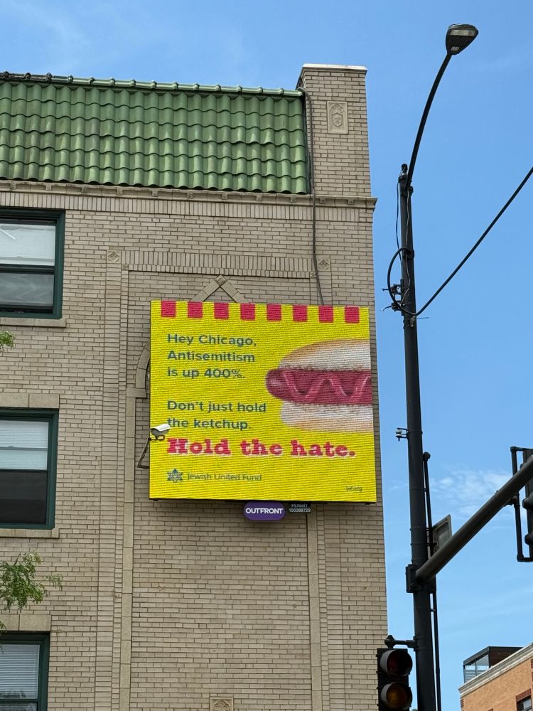 Digital sign on the side of a building that says “Hey Chicago, Antisemitism is up 400%. Don’t just hold the ketchup. Hold the hate.” There’s a picture of a hotdog with just ketchup on it. Ad is by the Jewish United Fund.